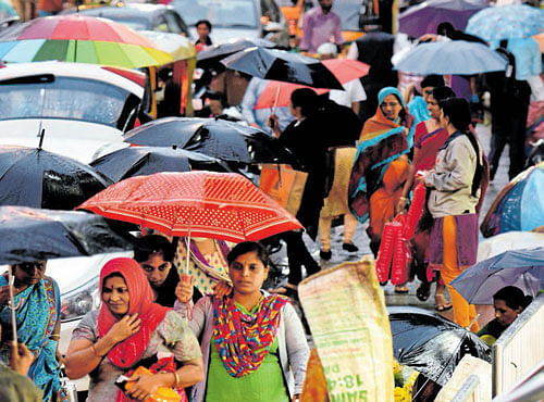 Deepavali shoppers protect themselves fromrain at the Malleswaram market on Monday. DH PHOTO