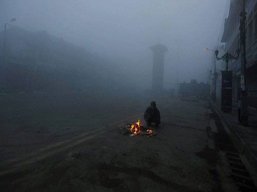 A man burns fire to warm himself during a foggy morning at Lal Chowk in Srinagar on Monday. PTI Photo