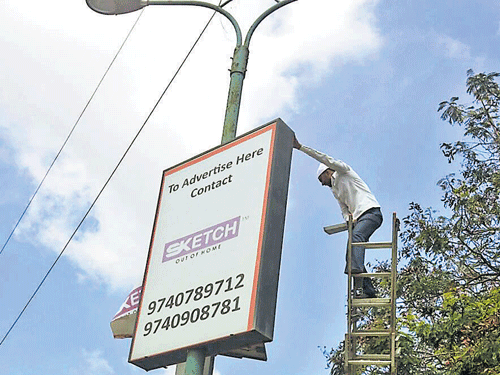 A BBMP worker clears an illegal pole advertising kiosk in Bommanahalli zone. dh photo