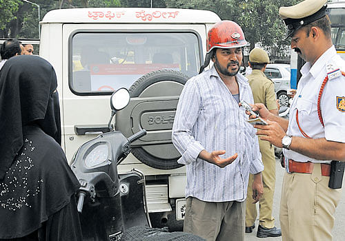 A traffic policeman books a pillion rider on Thursday for violating the helmet rule. DH PHOTO