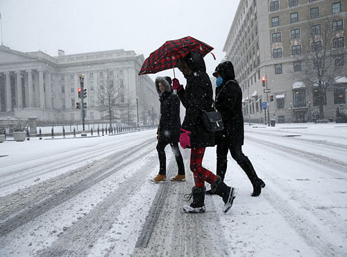 Women cross the street in the snow in Washington January 22, 2016. As much as 2 feet of snow is possible along the urban corridor extending from Washington to New York and Boston, the National Weather service said. REUTERS