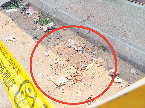 The blood stains covered with sand (circled), with the wooden bench on which Raju was sitting for the last time in the background, in front of the tea  shop, temporarily barricaded by the police,at Udayagiri in Mysuru. DH photo