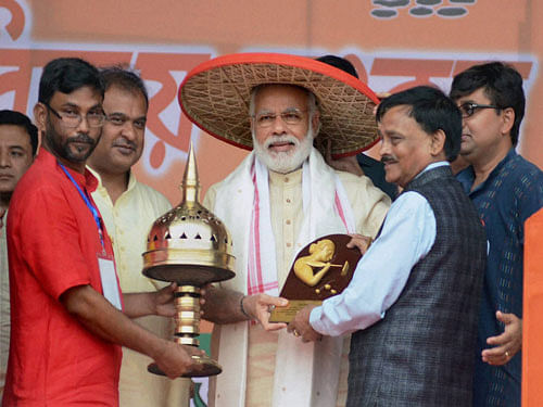 Prime Minister Narendra Modi being felicitated with traditional Japi (hat), Gomacha and Sarai during an election rally in Sonitpur on Sunday. BJP MP from Tezpur Ram Prasad Sarma (R) also seen. PTI Photo