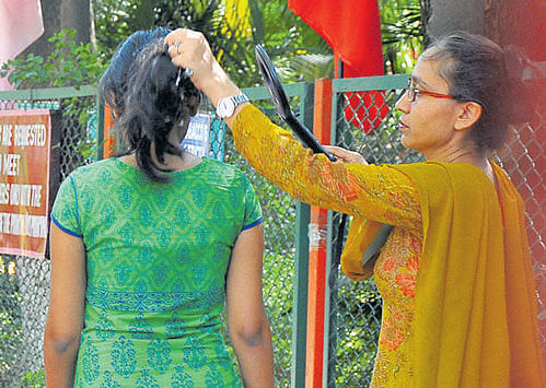 strict checking A woman searches a girl's hair and frisks another candidate during NEET-I at Kendriya Vidyalaya, Hebbal in Bengaluru, on Sunday. DH photo