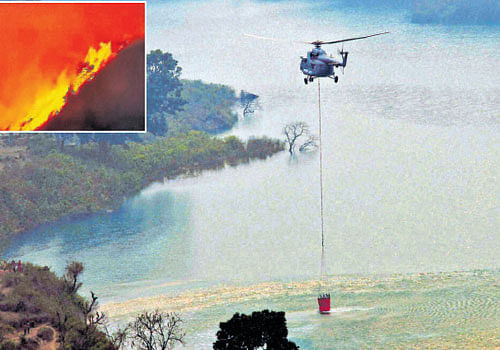An IAF helicopter collects water from Koteshwar dam during the operation to douse fire  (inset)&#8200;that broke out in the forests of Garhwal range in Srinagar, Uttarakhand, on Sunday. PTI