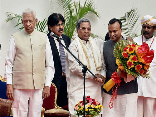 Karnataka Governor Vajubhai Rudabhai Vala looks on as Karnataka Chief Minister Siddaramaiah greets newly inducted minister Priyank Kharge during the swearing-in ceremony at Rajbhavan in Bengaluru on Sunday. PTI Photo.