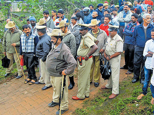People and police wait outside the mortuary to receive DySP M K Ganapathi's body in Madikeri on Friday. DH PHOTO