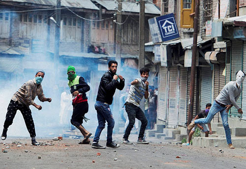 Protesters throw stones on police amid tear smoke during a clash in Srinagar on Sunday. Authorities imposed restrictions in most parts of Valley following the killing of most wanted Hizbul Mujahideen commander, Burhan Muzaffar Wani, along with his two associates. PTI Photo