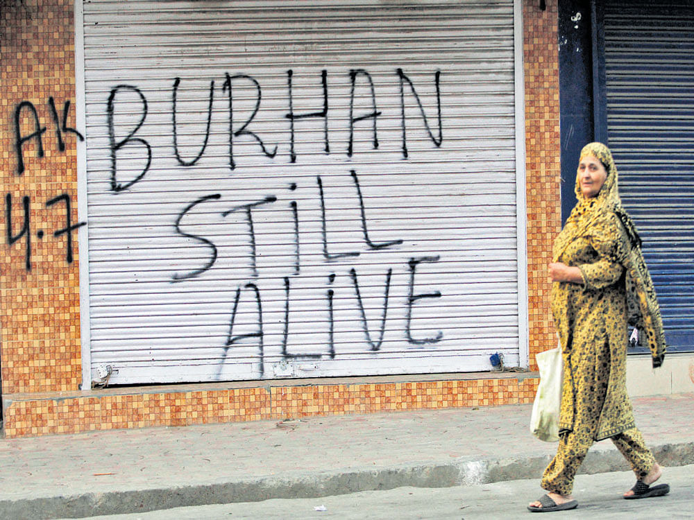 A woman walks past a closed shop painted with graffiti during a curfew in Srinagar on Monday. Reuters