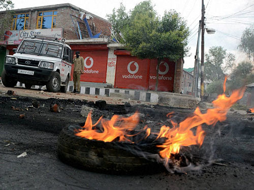 A security Jawan on a street where a tyre burning while protester defy curfew during curfew in Srinagar on Saturday. PTI Photo