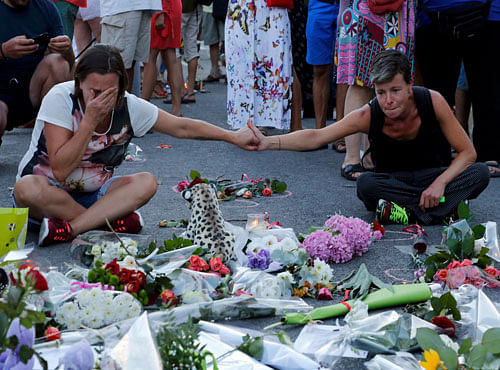 People react near flowers placed on the road in tribute to victims, two days after an attack by the driver of a heavy truck who ran into a crowd on Bastille Day killing scores and injuring as many, in Nice. Reuters photo