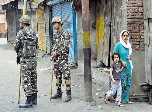 WATCHFUL:A woman and her child walk past soldiers standing guard during curfew and srike in Srinagar. The curfew was in place for the ninth consecutive day on Sunday. PTI
