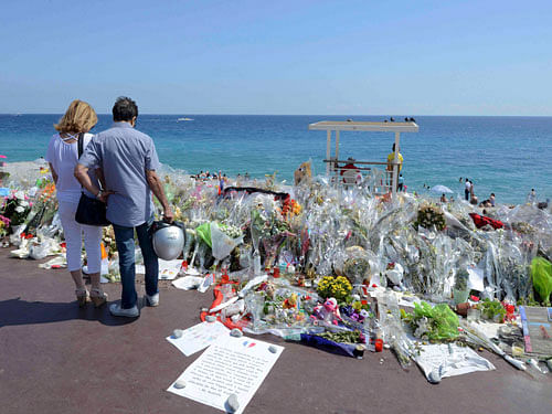 People stop near flowers left in tribute at a makeshift memorial to the victims of the Bastille Day truck attack along the Promenade des Anglais in Nice. Reuters Photo.