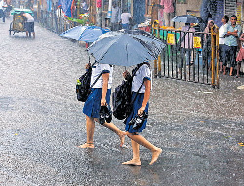 Students walk barefoot as they cross a waterlogged road in Kolkata. PTI Photo