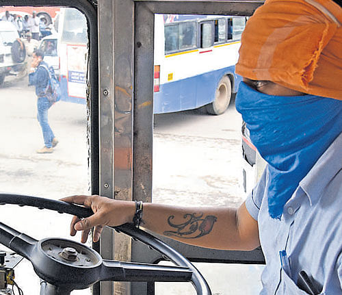 Fear of reprisal: Policemen guard a bus at the Kempegowda bus stand. (Right) A driver covers his face to conceal his identity as the BMTC&#8200;resumed  skeletal service from Shanthinagar to Majestic. DH Photo