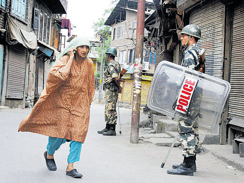 watching out: An elderly woman walks past security personnel standing guard during curfew in Srinagar on Sunday. PTI
