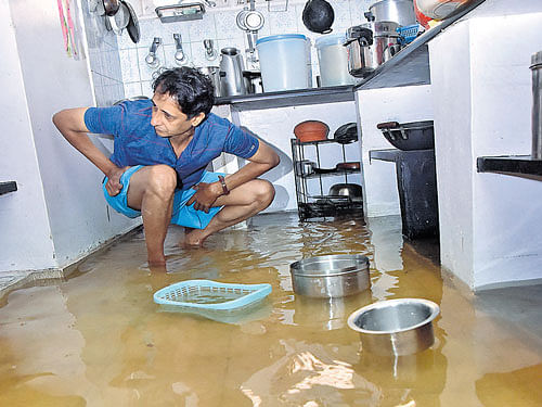 Kishore, a resident of Ashwathnarayana Layout, rearranges the kitchen in his house which is flooded with rainwater for the past three days.  DH photo