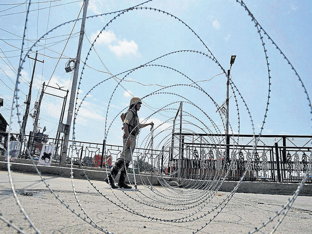 A security jawan stands guard during a curfew in Srinagar on Monday. PTI