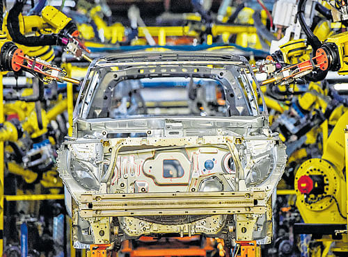 EFFICIENT RIDE: In this handout photo, adhesive is applied to a 2017 GMC Acadia and to its rear door striker latch plate (inset) on the framing line at the General Motors manufacturing plant. This will help make it 700 pounds lighter than the version it replaces. NYT
