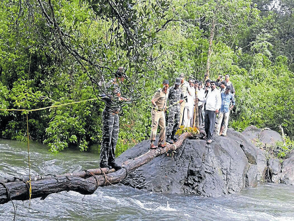 Superintendent of Police Bhushan Gulabrao Borase crosses an overflowing stream to reach Atrinje in Sulkeri GP of Belthangady taluk on Wednesday.