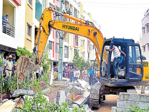 An excavator pulls down the compound wall of Suraksha Golden Palm apartment block at Avani Sringeri Nagar, Arakere, on Thursday. dh photo
