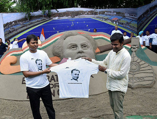 Former hockey player and MP Dilip Tirkey aand sand artist Sudarshan Patnaik unveil a jersey in front of a sand image created by the latter at a demonstration to demand Bharat Ratna honour for hockey legend Dhyan Chand, at Jantar Mantar in New Delhi on Sunday. PTI Photo
