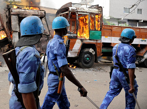 Police personnel move past a vehicle in flames during a protest by pro-Kannada activists on Cauvery water row, in Bengaluru on Monday. PTI Photo