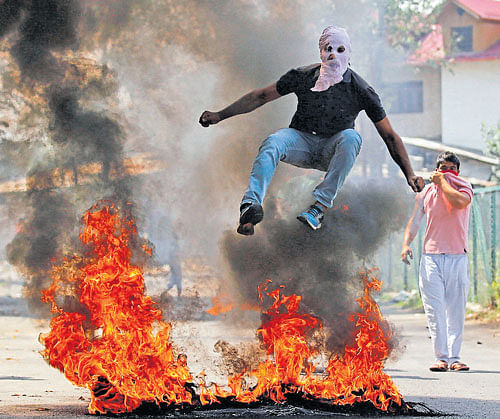 defiant: A man in a balaclava jumps over burning debris during a protest against the recent killings in the Valley, in Srinagar on Monday. REUTERS