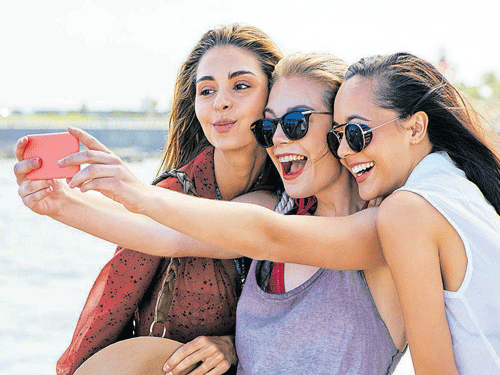 Three young girl friends taking picture of themselves on cell phone at  summer sunny day. Outdoor portrait of three friends taking photos with  smartphone Stock Photo | Adobe Stock