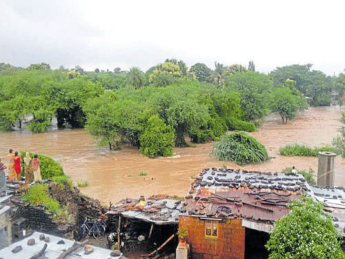 Residents stand atop an elevated place at the flooded Kalasadal village in Bidar taluk, after a percolation tank breached due to incessant rainfall in the past two days. DH photo