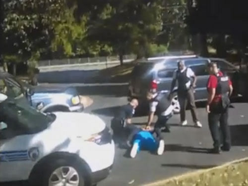 Four quick gunshots are heard, at which point the phone is pointing away from the shooting. Moments later, the video shows Scott lying face down on the asphalt surrounded by officers. Screengrab
