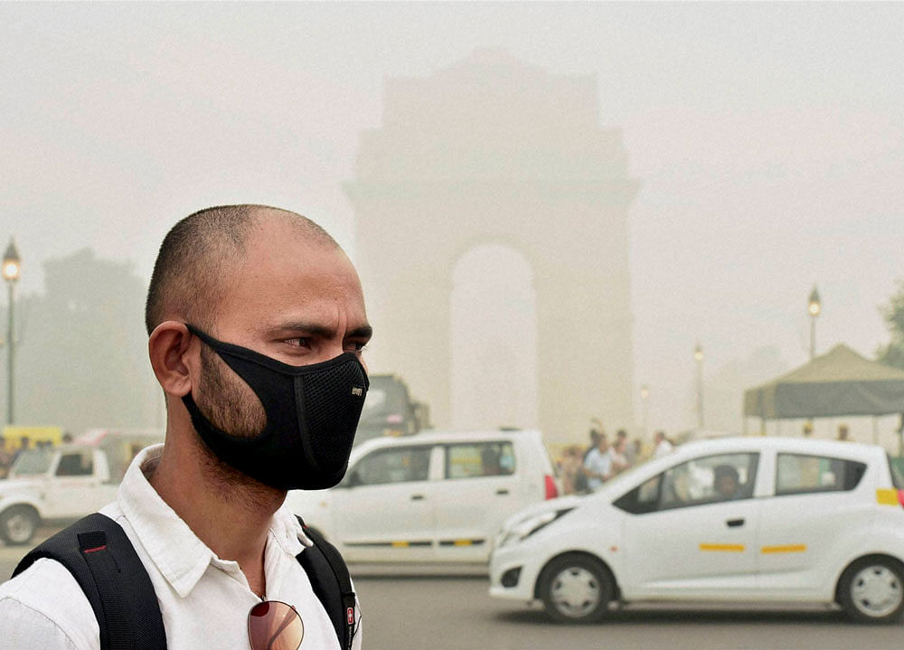 A man takes protection against pollution as smog covers India Gate in New Delhi on Sunday. PTI Photo