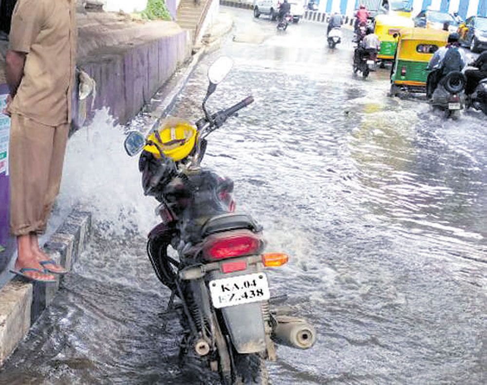 Drinking water overflows on the road near the entrance to the Palace Grounds at Vasanathnagar on Monday. DH Photo.