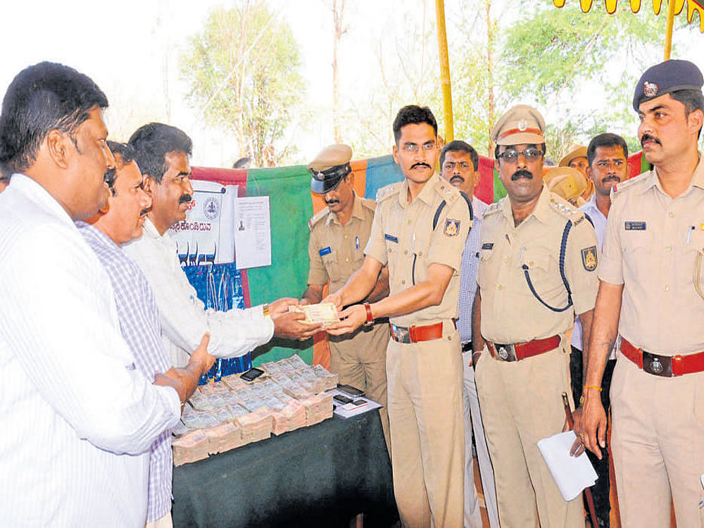 Superintendent of Police Kuldip Kumar R Jain hands over cash that was stolen at the KSRTC depot to authorities, during the property return parade in Chamarajanagar recently.