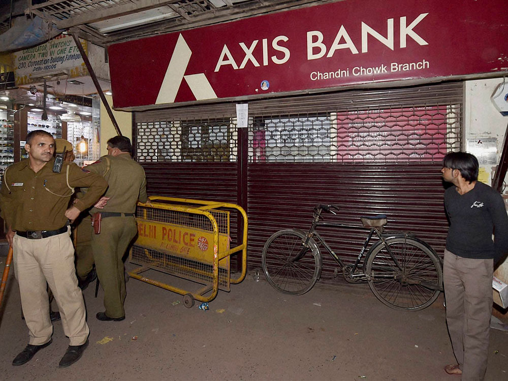 Police men guard outside an Axis Bank branch during a raid by Income Tax officials in the Chandni Chowk in New Delhi on Friday. The officials have found several fake accounts in the bank. PTI Photo
