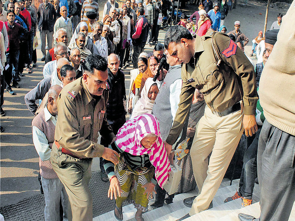 helping hand: An elderly woman is helped by policemen as people stand in queues outside a bank in Faridabad on Tuesday. PTI