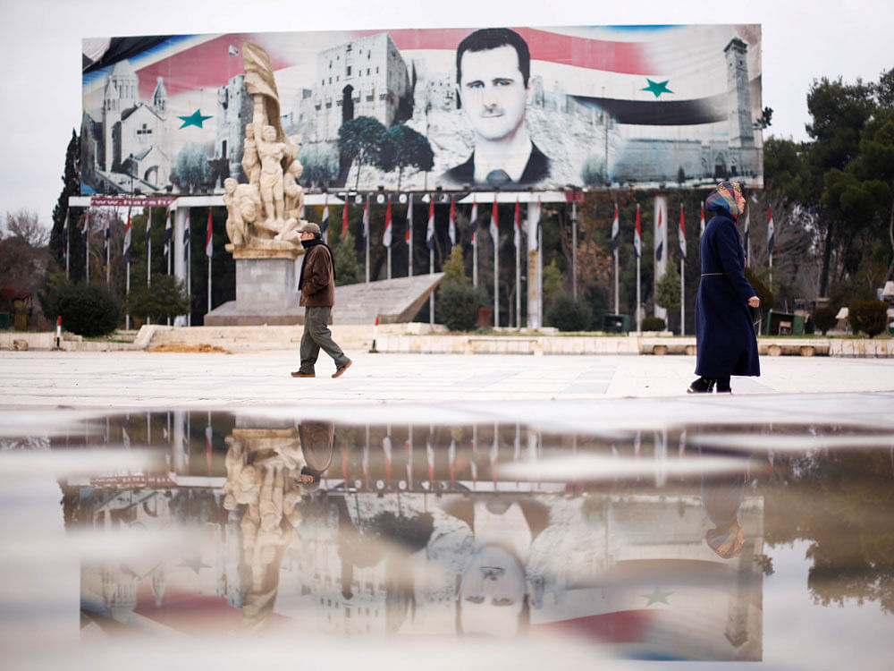 People walk past a billboard depicting Syria's President Bashar al-Assad at Saadallah al-Jabri Square, in the government controlled area of Aleppo, Syria December 17, 2016. REUTERS