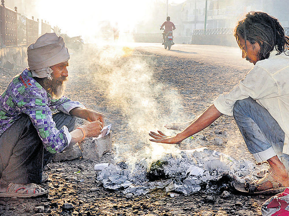 Daily wagers warm themselves on the roadside after setting garbage afire in Vijayapura on Saturday. dh photo
