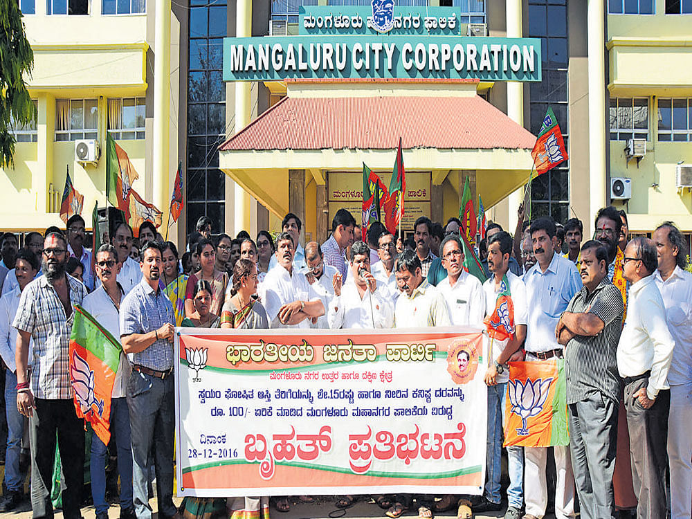BJP members stage a dharna in protest against the hike in&#8200;SAS in front of MCC in Mangaluru on Wednesday. DH photo