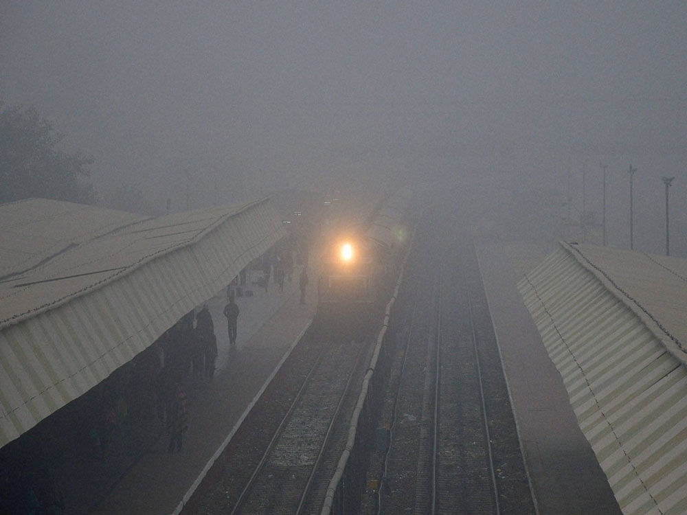 Passengers wait at a railway station as a train arrives amid dense fog, in Bikaner on Saturday. PTI Photo