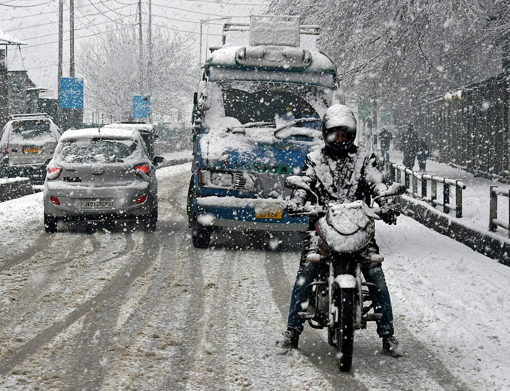 A motorcyclist tries to balance his two wheeler while moving cautiously during snowfall in Srinagar on Friday. PTI Photo