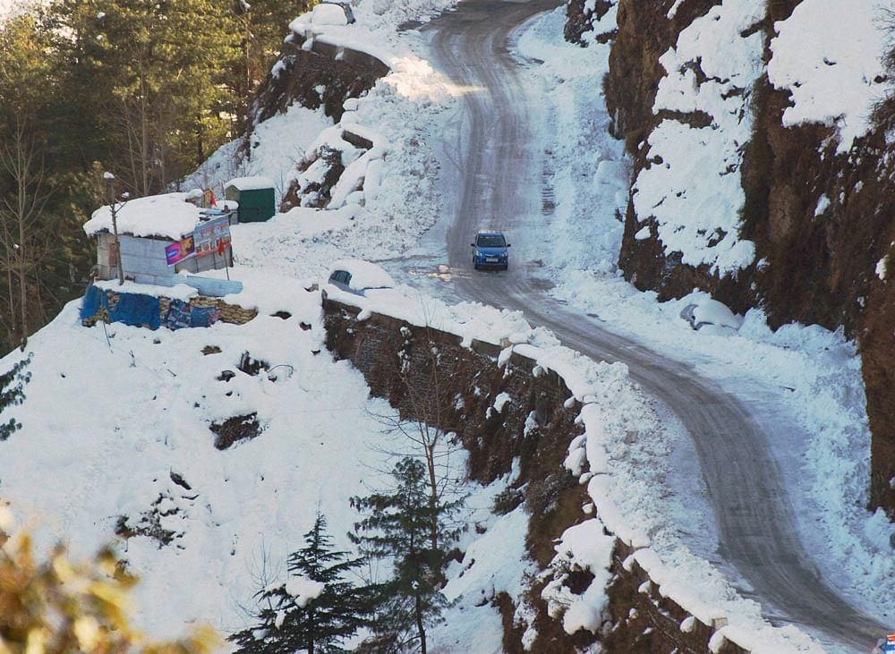 A vehicle moves slowly on a snow-covered road following heavy snowfall at Sanjoli in Shimla on Thursday. PTI