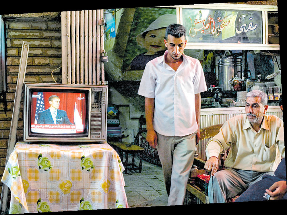 bound by legacy: In this 2012 file photo, people watch US President Barack Obama's speech delivered from Cairo, Baghdad. While the drone programme began under Bush, Obama, styling himself as an anti-terrorist commander, substantially expanded it. nyt