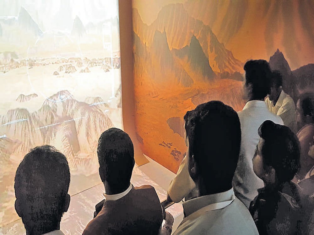 People are glued to a screen showing Martian surface at  a small theatre set up by Isro.