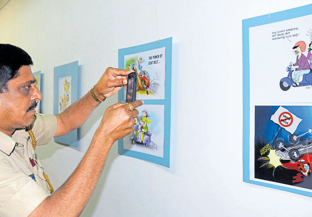 A transport official takes a picture of a cartoon at an exhibition of cartoons being held to  create awareness on vehicle accidents at Chitrakala Parishath. DH PHOTO