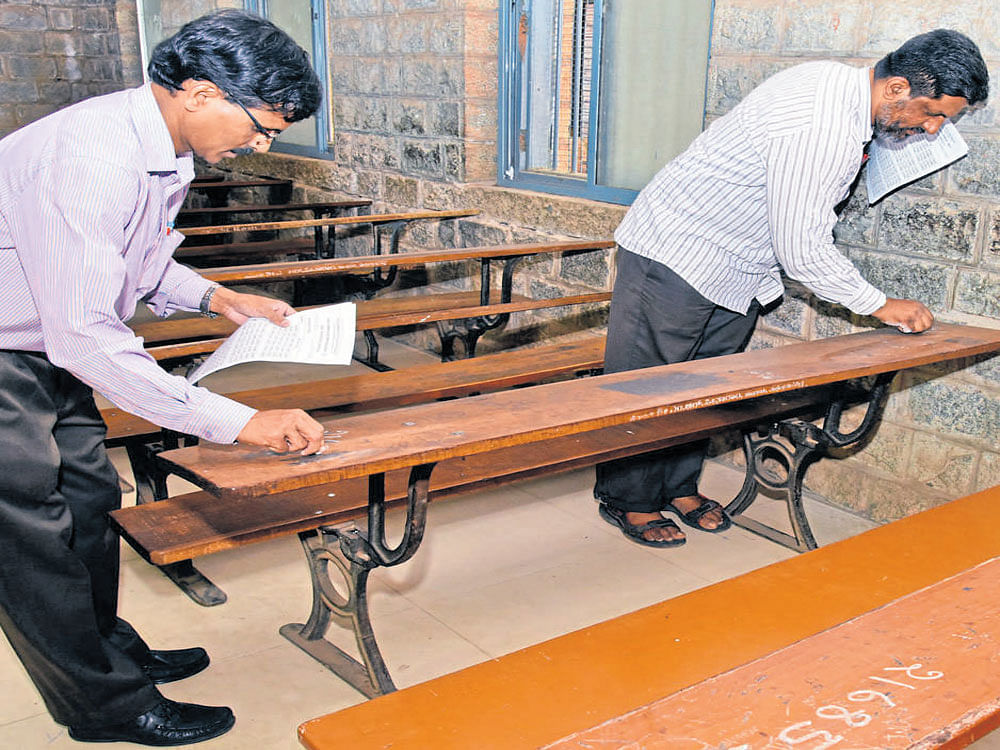 Teachers mark register numbers of students on benches for second PUC examinations at the Government Pre-university College for Boys at Malleswaram  in Bengaluru on Wednesday.  The examinations start on Thursday. DH photo