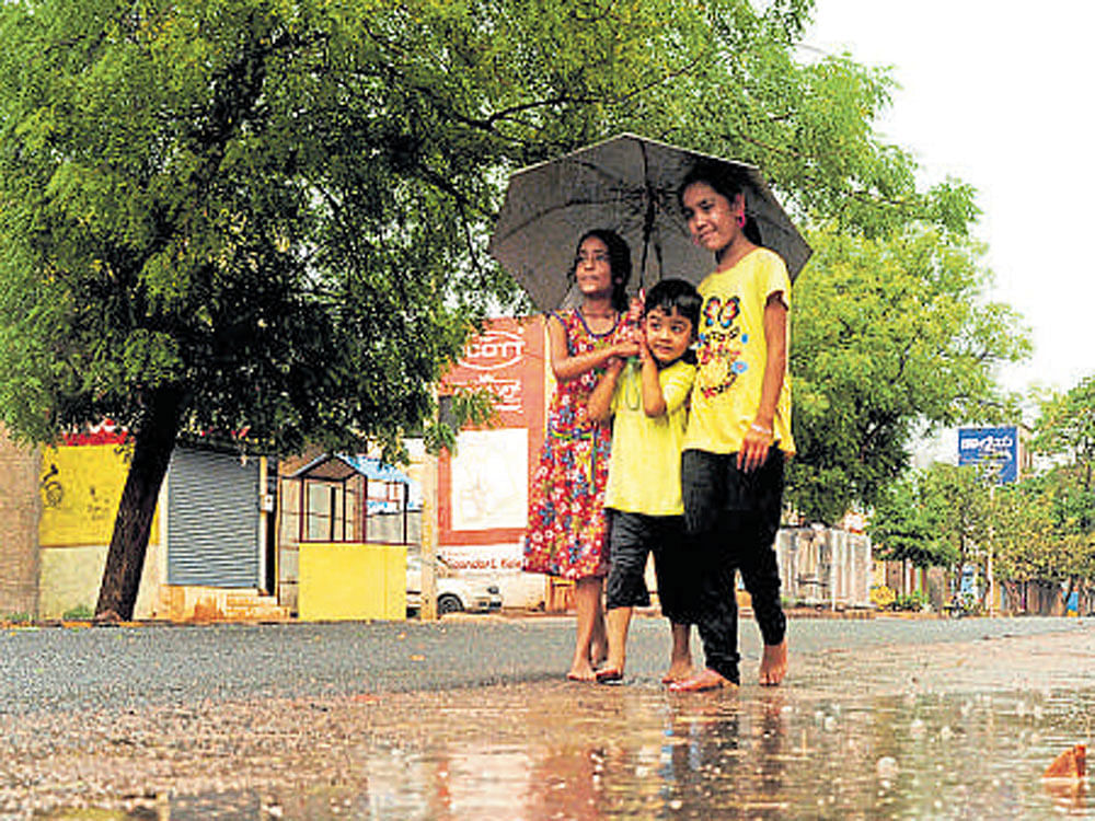 Children walk in rain with an umbrella in Bagalkot on Wednesday. DH photo