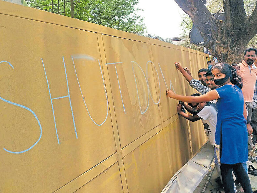 Protesters scribble a message on the compound wall of the KCDC&#8200;plant in Somasundarapalya on Sunday, demanding its closure. DH Photo