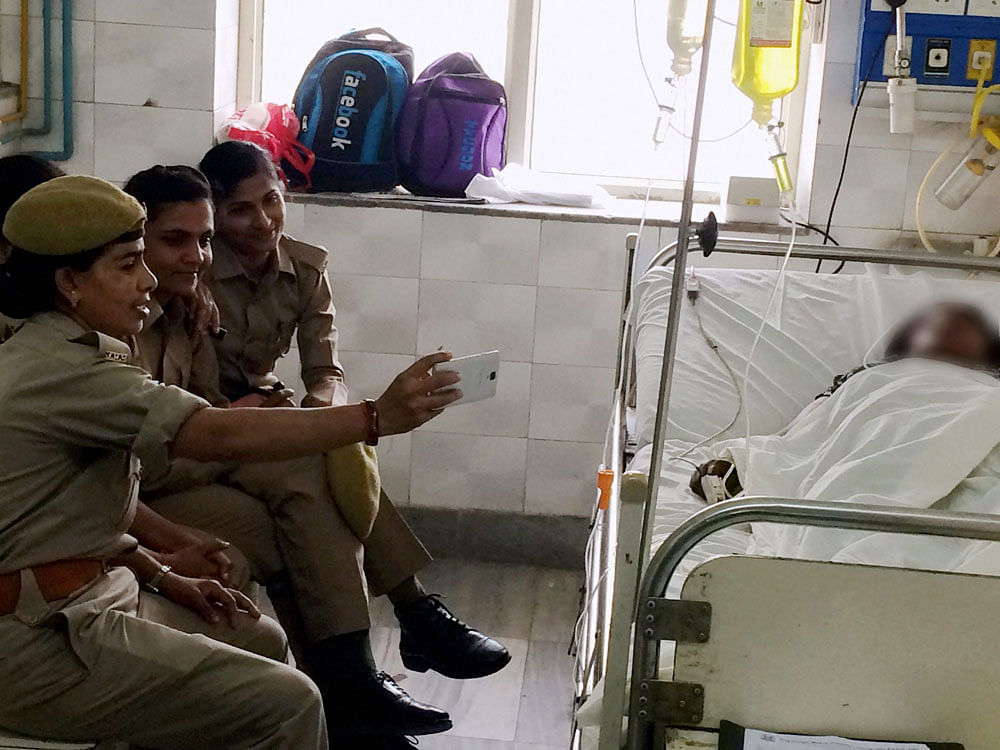 Insensitive: Woman constables, posted for the security of an acid attack survivor, take  selfies on Friday. She is being treated at Lucknow's King George's Medical University. PTI