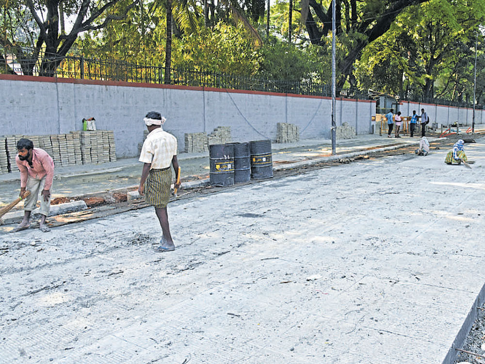 Workers on Saturday give finishing touches to the right side of Nrupathunga Road which has been concretised. DH Photo